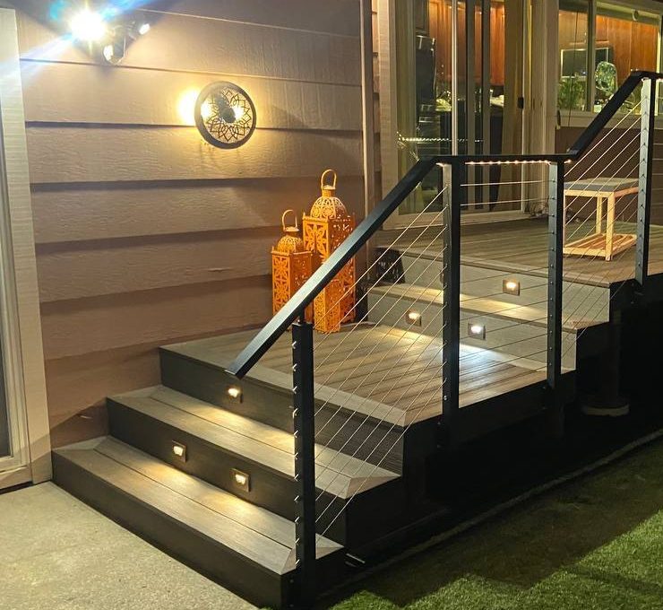Composite deck stairs at night with lights in the risers, an LED strip under the top rail and a wall light by the door