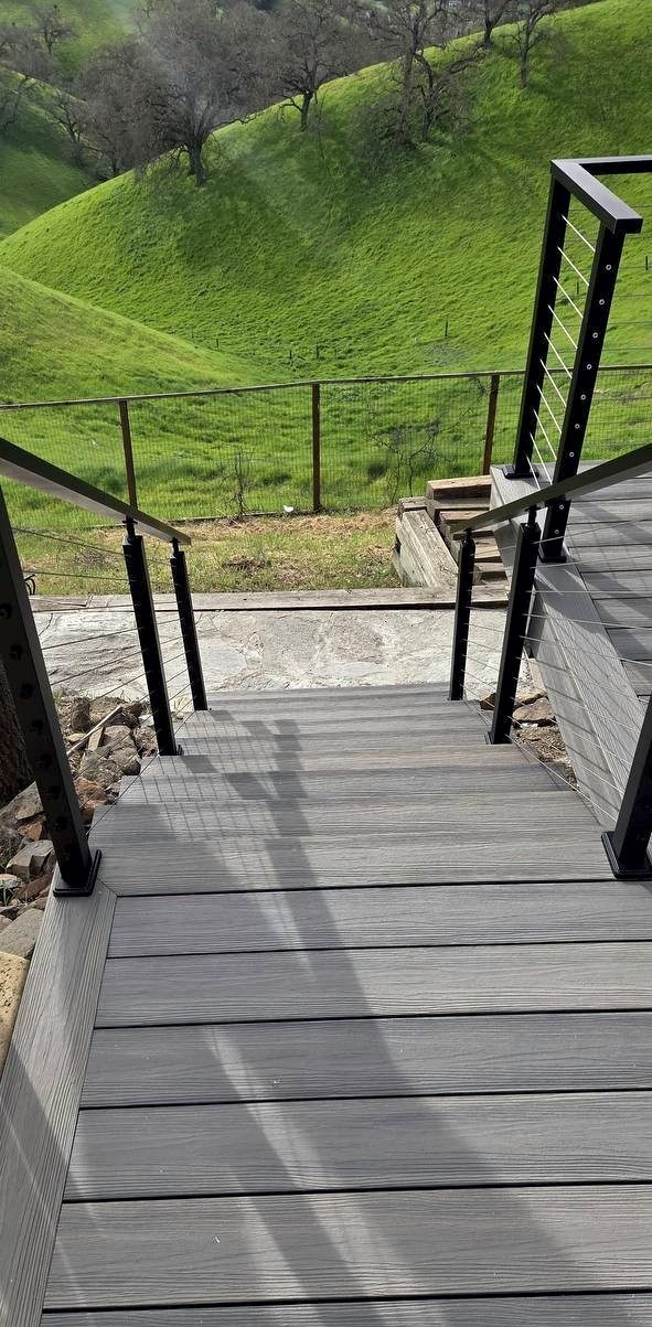 Composite deck stairs with black powder-coated aluminum cable railing going down a slope
